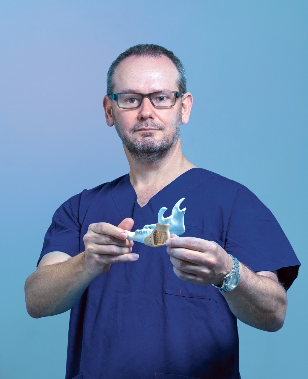 Professor Jonathan Clark in scrubs in front of a blue background, holding a 3D printed mouth piece