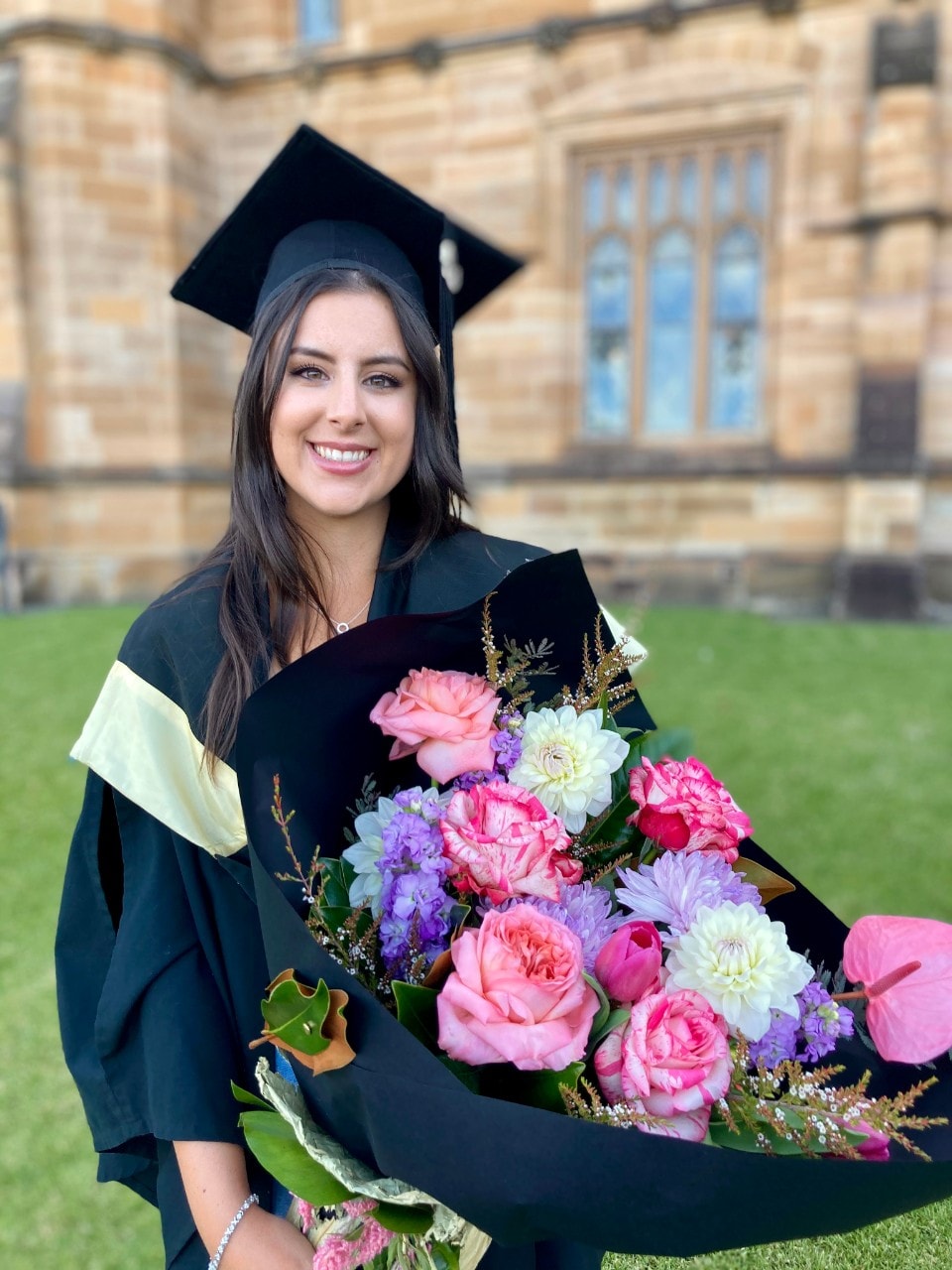 Maddi Eveleigh at her graduation ceremony, wearing graduation regalia and holding a bunch of flowers