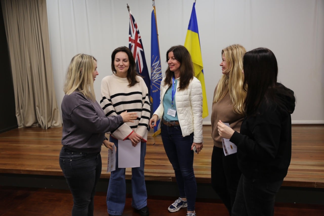 A group of women speaking in front of the Australian and Ukraine flags