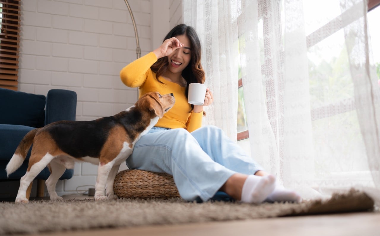 A woman sitting on the floor with her dog having a coffee break