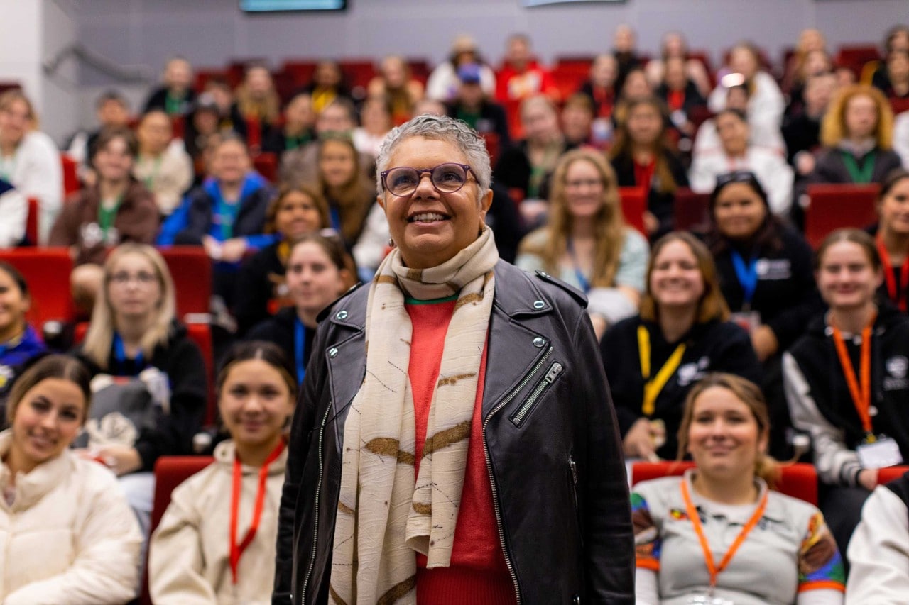 Deborah Cheetham Fraillon standing in front of a group of high school students in an auditorium.
