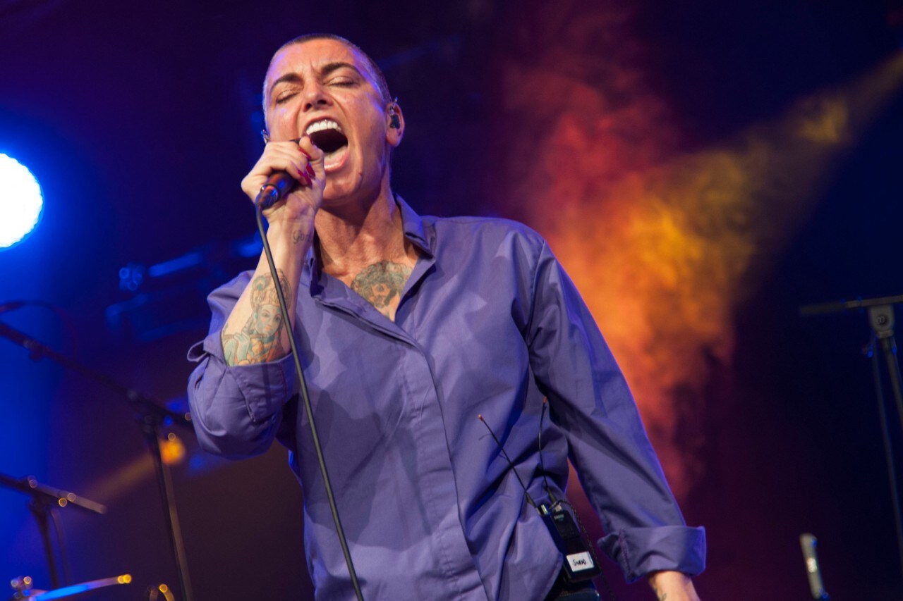 Sinead O'Connor singing into a microphone on stage.