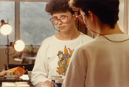 A younger Lisa Jackson Pulver looking into a mirror so that her reflection looks back at the camera. She has short hair and glasses.