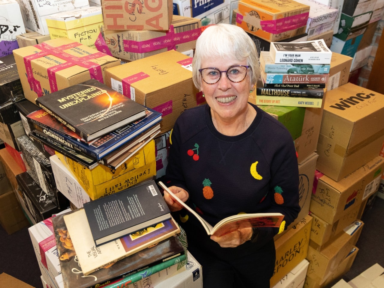 Maggie McElhill surrounded by boxes of book donations smiling up at the camera