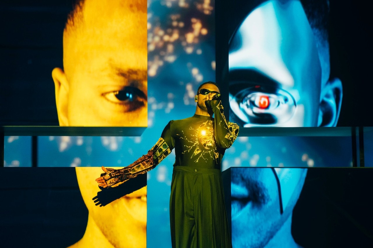 a male singer in front of a giant face with the Ukraine colours on it