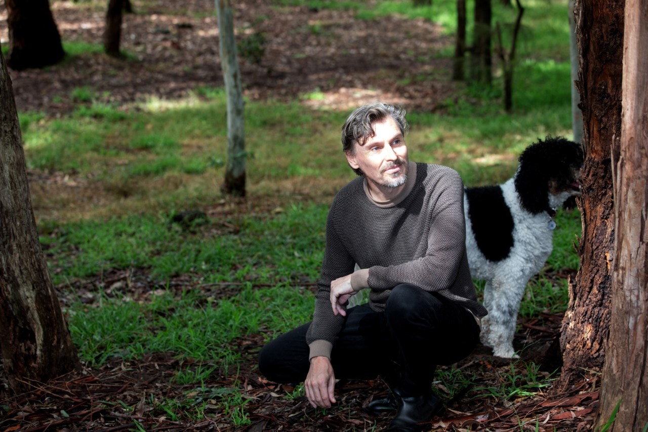 Michael Harvey crouching next to a tree with his black and white dog.
