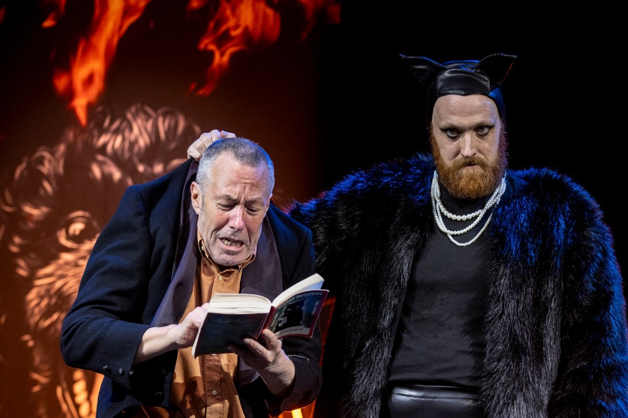two actors on stage, one is dressed as an evil black cat and is holding the other by the neck