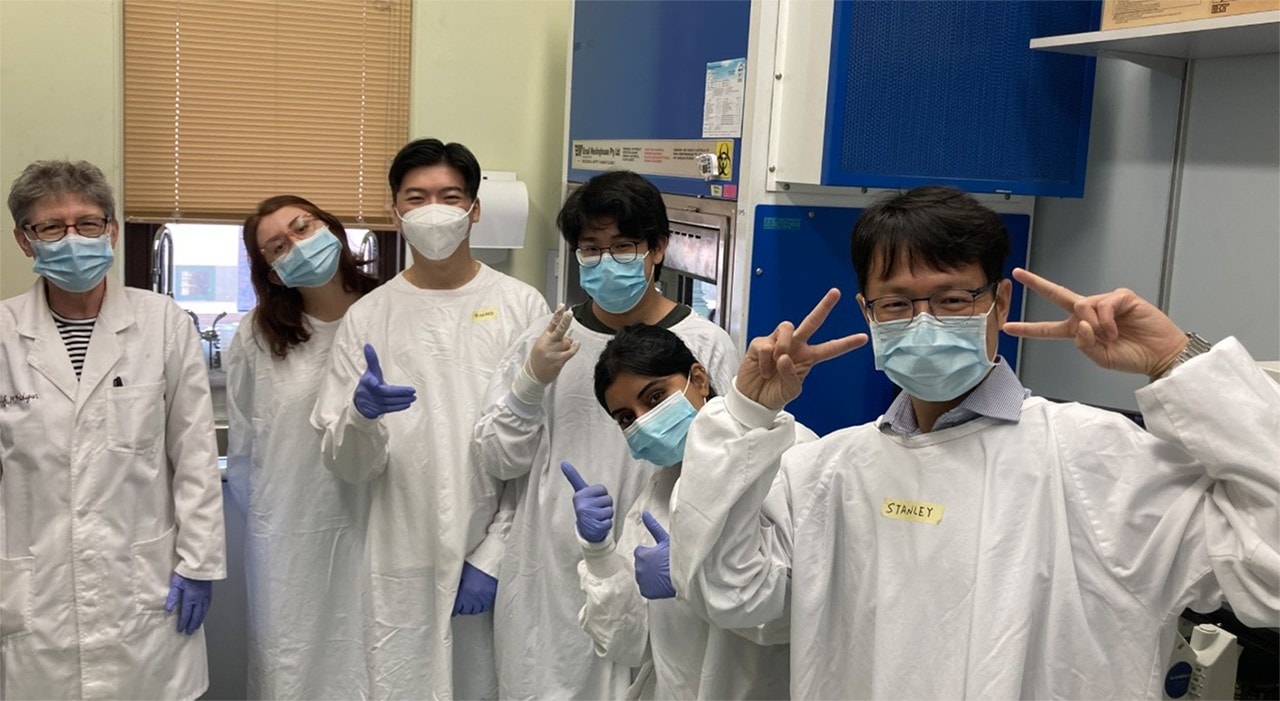 A group of summer research students in the lab making peace signs with their hands.