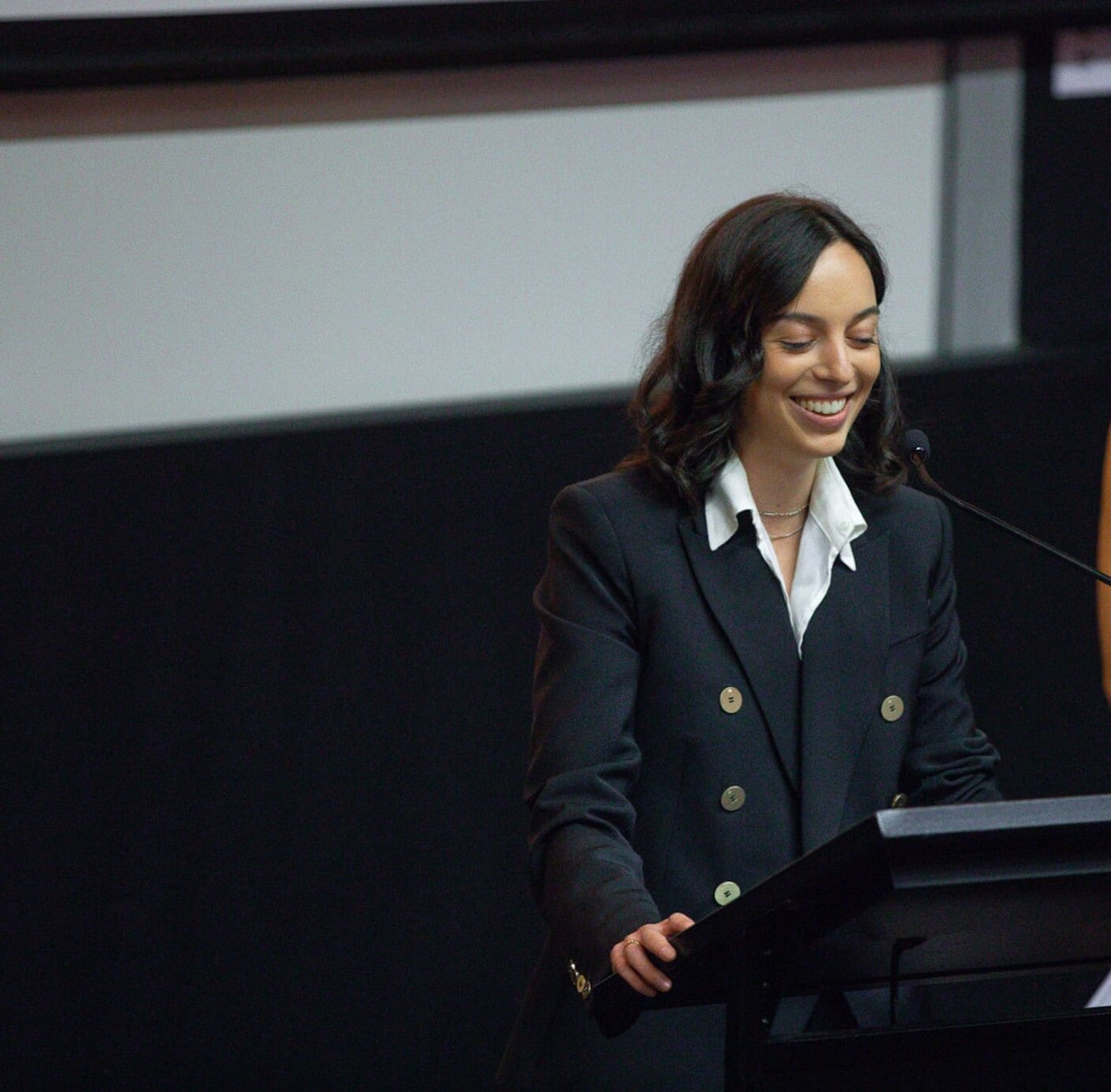 Olivia Morris wearing a black jacket and standing in front of a lecturn to give a speech
