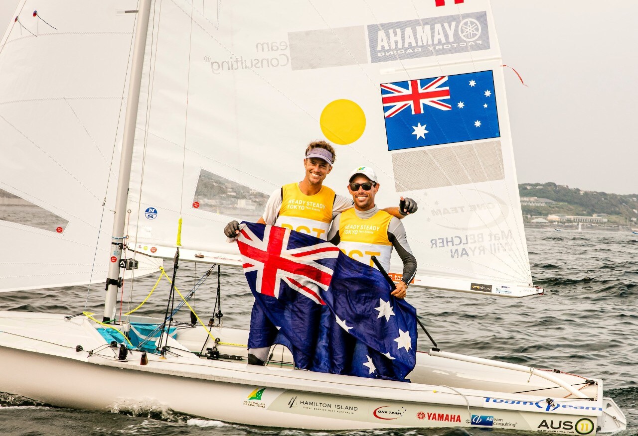 Two men stand on yacht wearing yellow vests and holding Australian flag