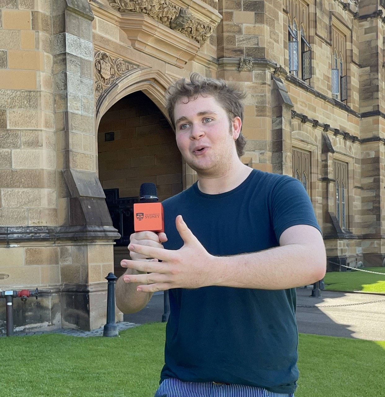 First year student Will standing at the front of the Main Quadrangle with a microphone