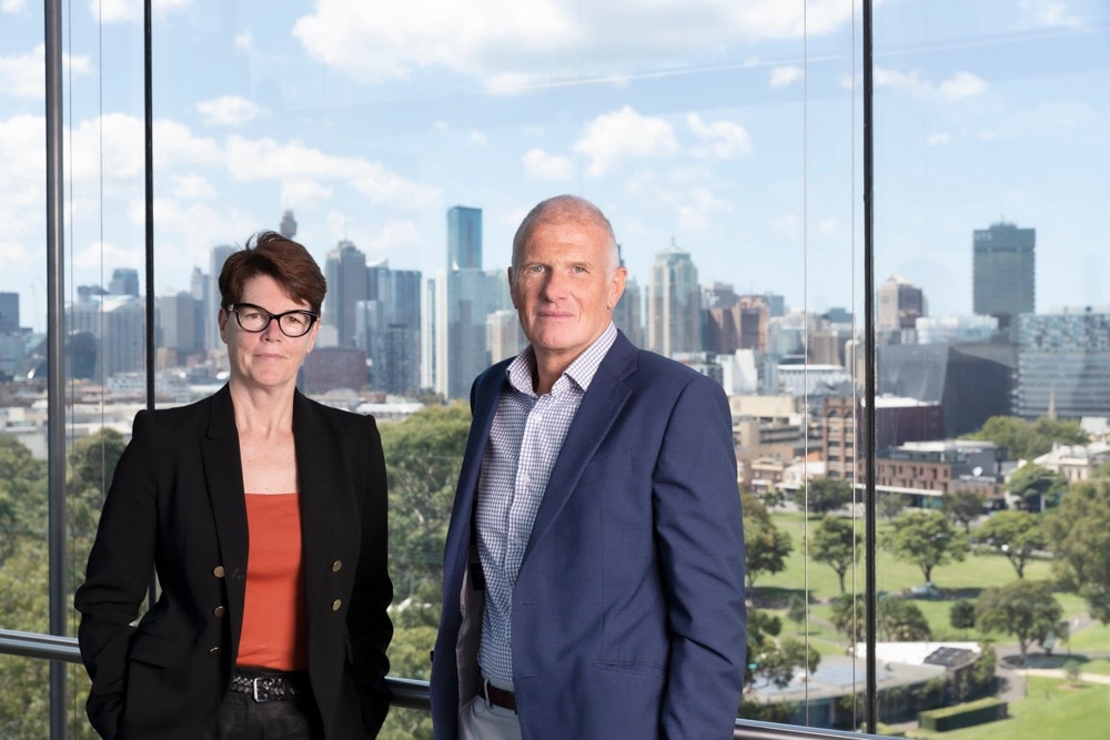 Dr Kym Sheehan and Professor David Kinley standing on the top floor of the Sydney Law School, with the Sydney CBD in the background.