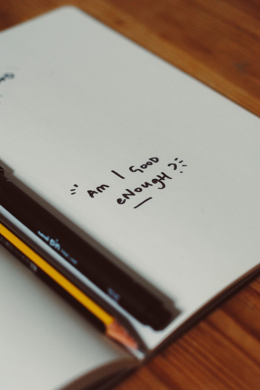 Open notebook with handwritten text 'Am I good enough?' written on the page